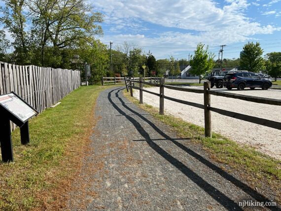 Gravel parking lot and fence next to a rail trail.
