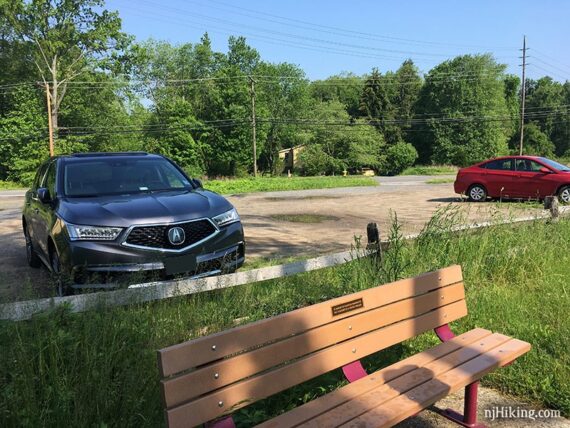 Bench in front of a small dirt parking lot for a trail