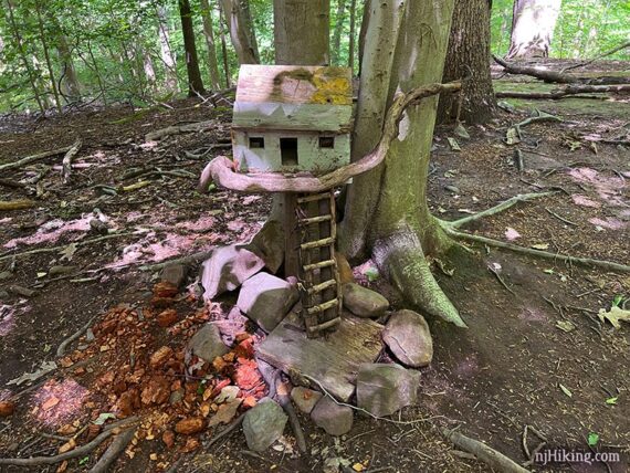 Wooden fairy house sitting on a branch with a ladder leading up to it.