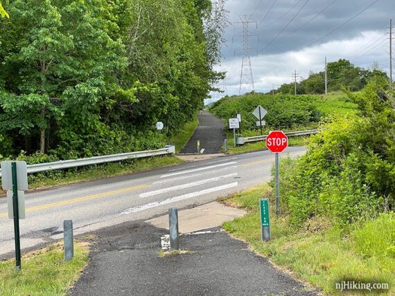 Rail trail at a road crossing with trees on one side and power lines on the other