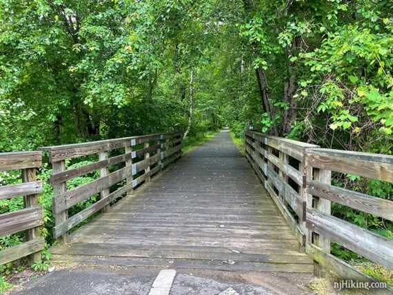 Large wooden bridge with green trees arching above it.