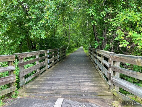 Large wooden bridge with green trees arching above it