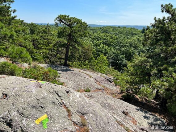 Yellow and green trail markers on a rock slab with view of mountain beyond