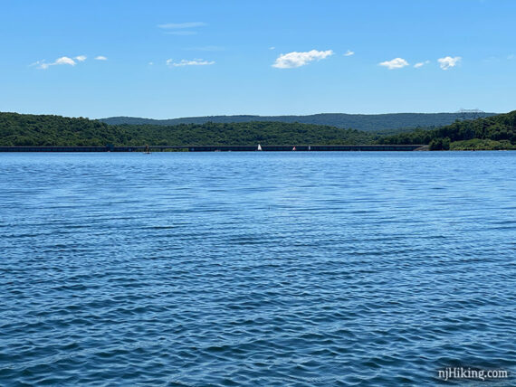 Rippled blue lake with a sailboat and dam in the distance.