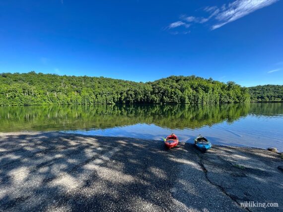 Two kayaks on a paved boat ramp with green hills and blue water beyond.