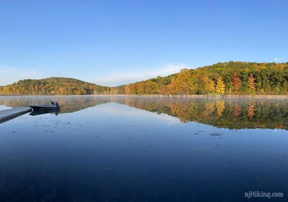 Boat at a dock with hills in the distance reflected in the water.