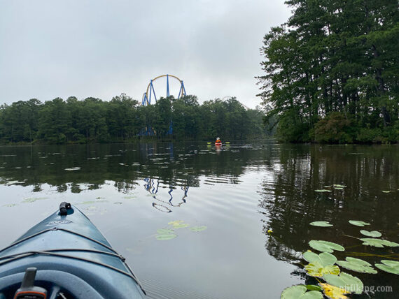 Kayaks on a lake with a roller coaster in the distance.