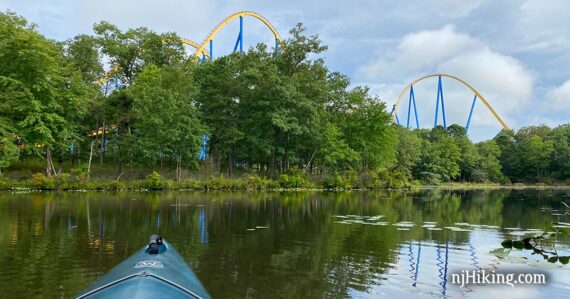 Kayak on a lake with Nitro roller coaster seen in the trees beyond.