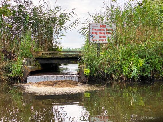 Narrow strip of land with a spillway and no trespass sign.