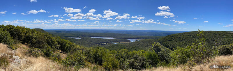 View from Raccoon Ridge of Lower Yards Creek reservoir in the valley below with a bright blue sky and fluffy clouds.