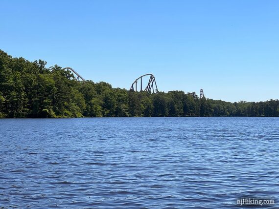 The tops of a roller coast seen above trees along a lake.