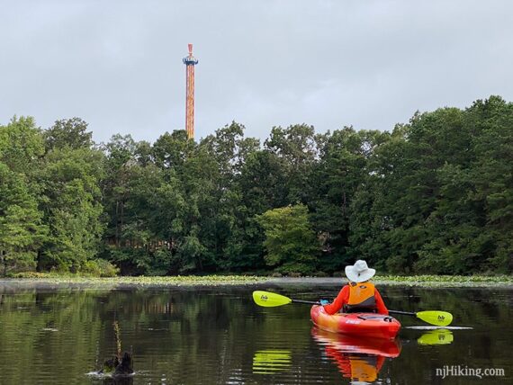 Tall tower with a Six Flags sign on top and a kayker on a lake in the foreground.