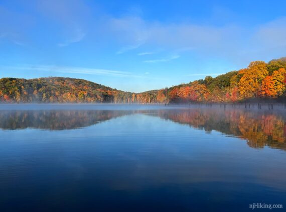 Yellow and orange colored hills lit by sunlight beyond a lake.