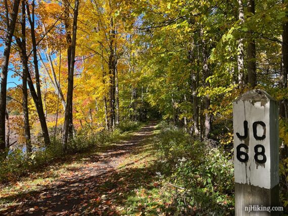 Fall color along a rail trail near a wooden marker with "JC 68".