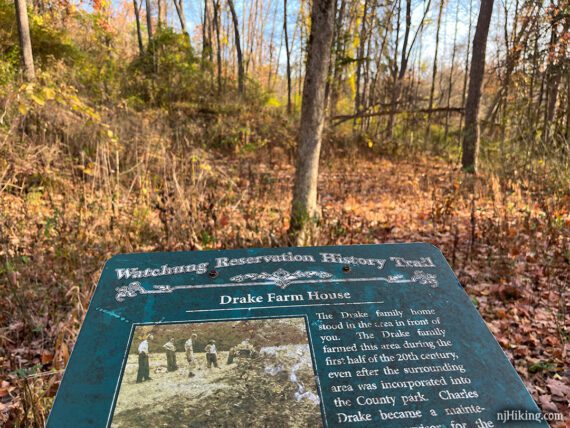 Sign about the Drake Farm House in front of an open area with overgrown house foundation.