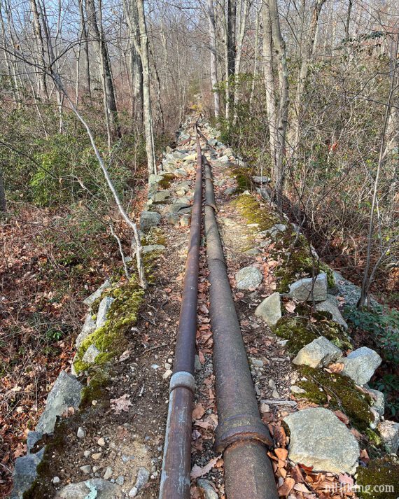 Trail running next to old metal pipes on a raised rocky berm.