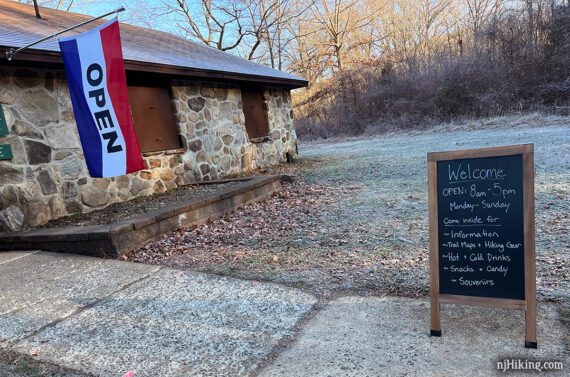 Chalkboard sign with hours and information posted outside a visitor center with an open flag.