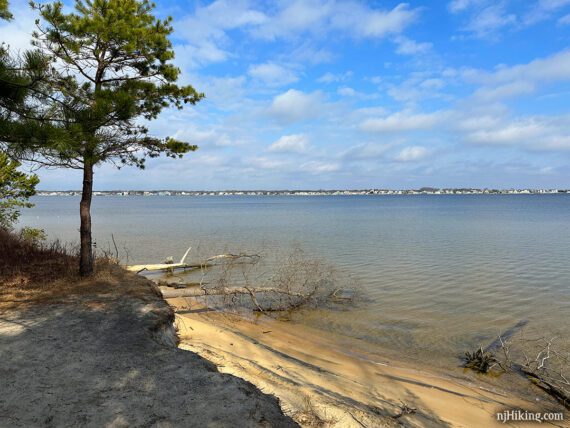 Viewpoint from a sandy embankment overlooking houses beyond water.