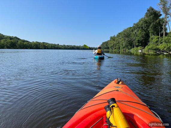 Kayaker on a blue lake with the bow of an orange kayak visible.