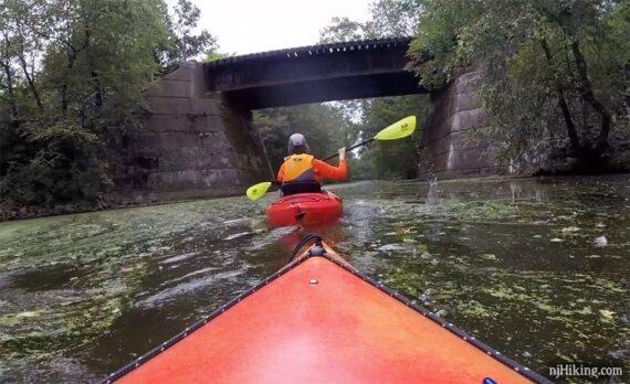 Kayaker going under a train bridge.