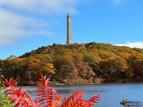 High Point Monument on a fall foliage covered hill with a lake in the foreground.