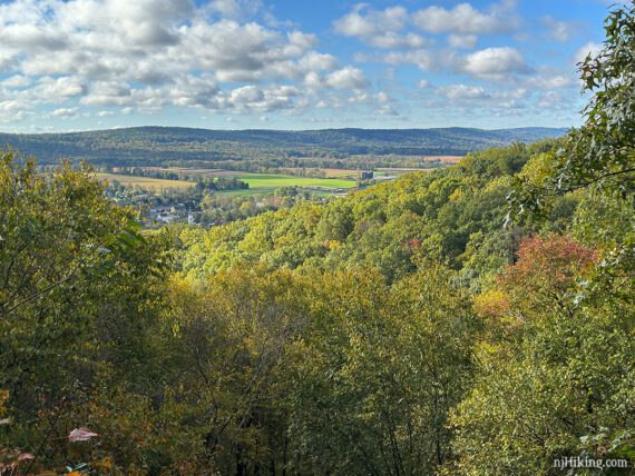 Zoom into farms and fields in a valley below a viewpoint.