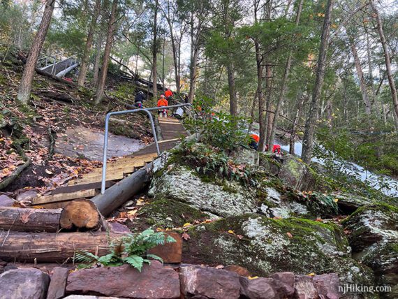 People in orange jackets on steep stairs next to a tall waterfall.