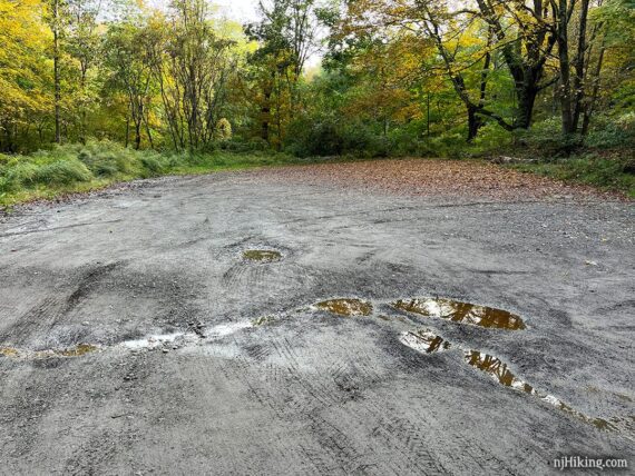 Small dirt trailhead parking lot with puddles.