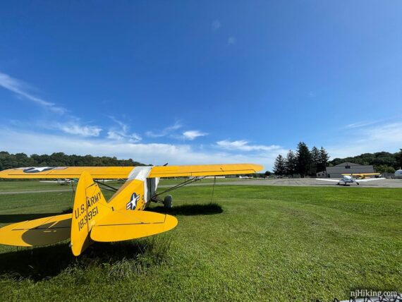 Yellow Army small plane on a large grassy field in an airport.