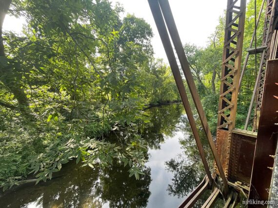 Looking over the side of a metal bridge to a stream.