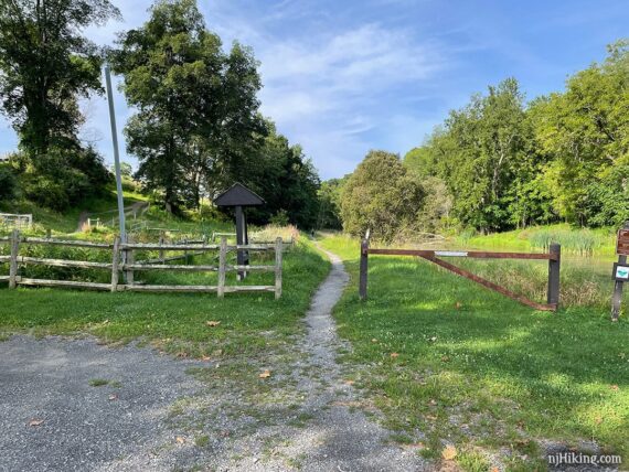 Small gravel and dirt lot with a rail-trail running through a break in a fence.