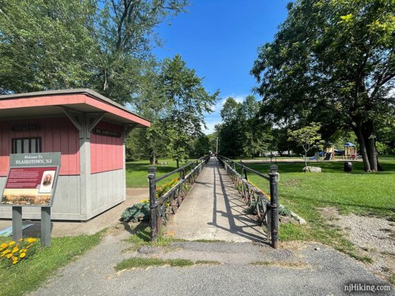 Small red building and information plaque next to a long concrete bridge over grass.