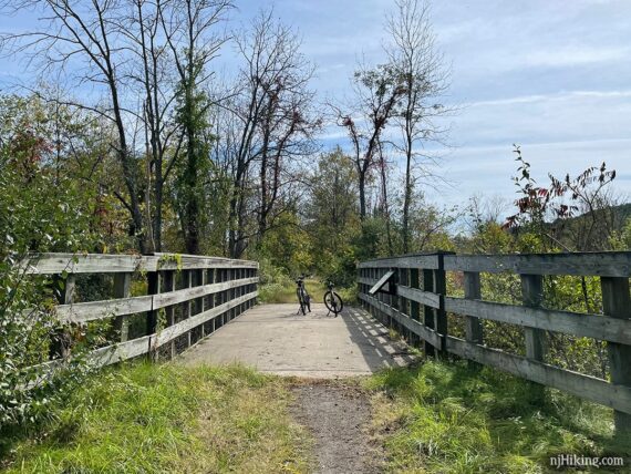 Two bikes on a wide wooden bridge over a small river.