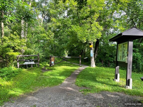 Rail trail path with a park gate, kiosk, and signs.
