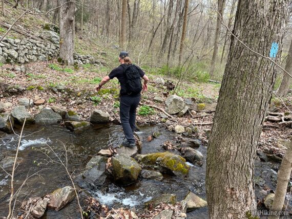 Hiker hopping rocks across a stream.